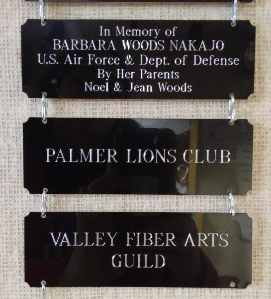 3 black metal plaques hung in a vertical row with engraving. 